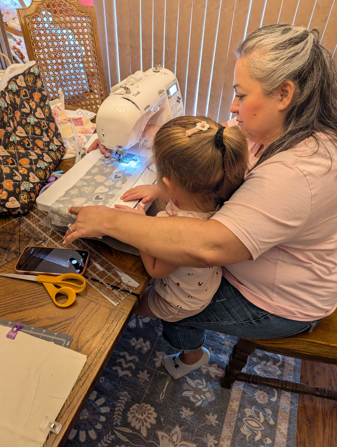 Elam & Co. maker hand-guiding fabric through a sewing machine to hand-quilt a bag, with her granddaughter Aliyah