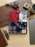 Bandana Patchwork iPad Sleeve featured in Bandana Patchwork Ipad Tote.png showcasing a diamond-quilted tablet cover in red, white, and navy paisley block prints resting on a wood board next to a tablet, fountain pens, and dried flowers.