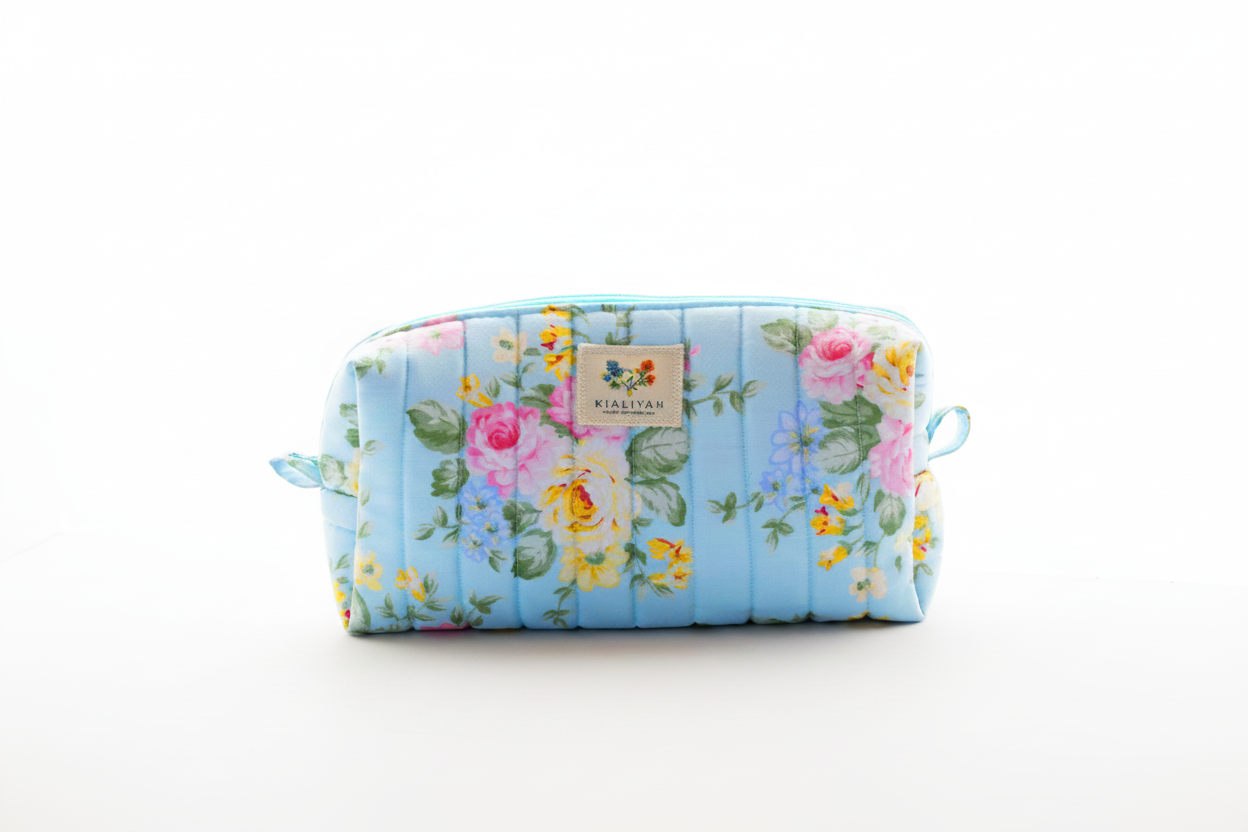 The English Rose Quilted Makeup Bag featuring a vintage pink and yellow floral print on sky-blue cotton fabric, designed with vertical channel quilting, a flat stand-up base, and a gold-tone zipper with a matching fabric pull-tab.