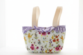 The Wildflower & Gingham Ruffle Stroller Tote featuring a pink and purple wildflower print on white canvas, detailed with a purple gingham ruffled collar, wide cream handles, and a centered white KIALIYAH label.