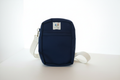 Navy blue canvas sling bag with off-white strap and brass hardware on a white background.