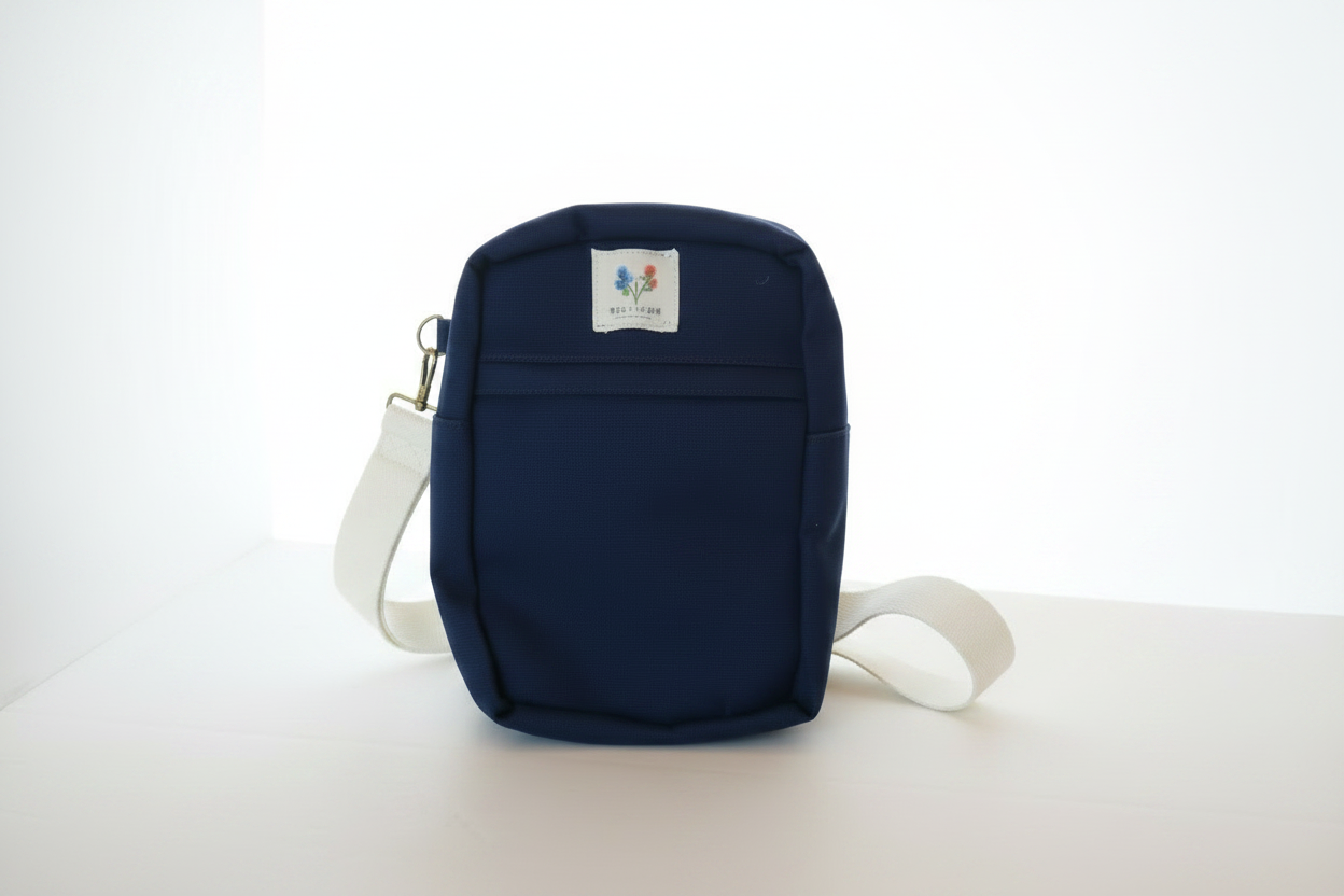 Navy blue canvas sling bag with off-white strap and brass hardware on a white background.