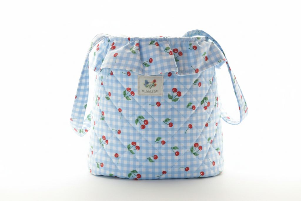 Light blue quilted stroller organizer bag featuring a red cherry print, a gathered ruffle top, and wide fabric handles.