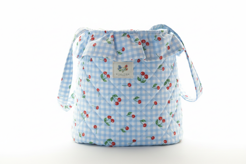 Light blue quilted stroller organizer bag featuring a red cherry print, a gathered ruffle top, and wide fabric handles.