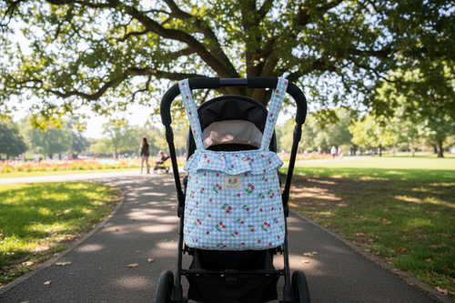 The Cherry Gingham Quilted Stroller Bag featuring a cherry print top with red and white gingham base, a gathered ruffle drawstring closure, padded diamond-quilted body, and stroller-ready straps.