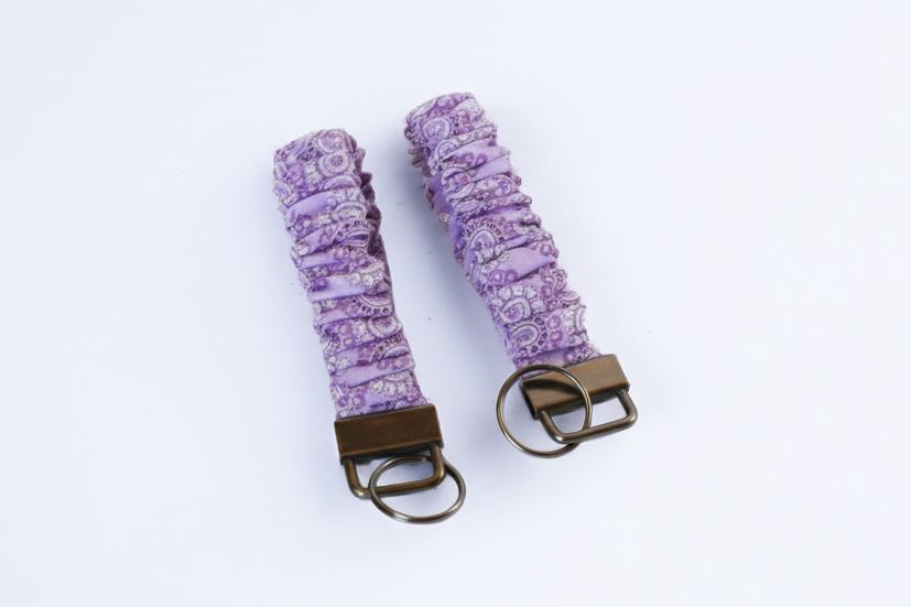 Two purple patterned keychains with brown metal clasps on a white background