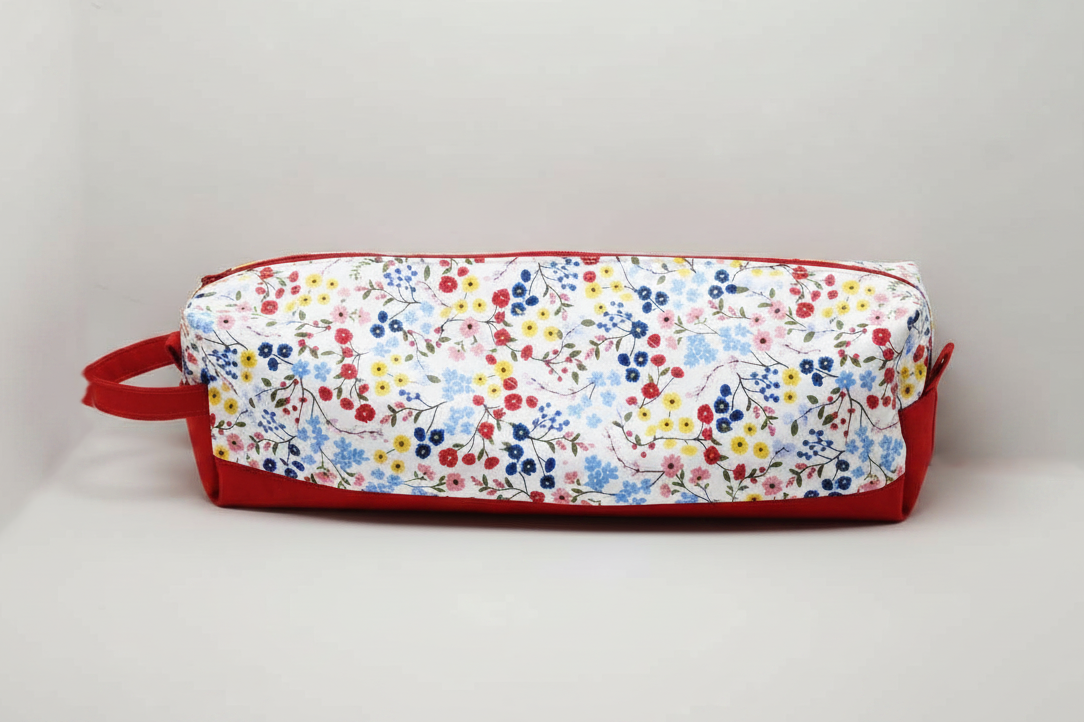The Vibrant Floral Hot Tool & Travel Bag featuring a pink, purple, and amber botanical print on white cotton fabric, designed with vertical channel quilting, a gold top zipper with a matching fabric pull-tab, a side hand strap, and a centered white KIALIYAH label.