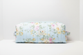 The English Rose Quilted Hot Tool & Travel Bag featuring a vintage pink and yellow floral print on sky-blue cotton fabric, designed with vertical channel quilting, a gold top zipper with a matching fabric pull-tab, a side hand strap, and a centered white KIALIYAH label.