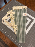 Sage Plaid and Blossom Bouquet Wrap canvas flower carrier featuring a sage green and white plaid pattern with yellow floral ruffles and cream shoulder straps on a gray cutting mat.