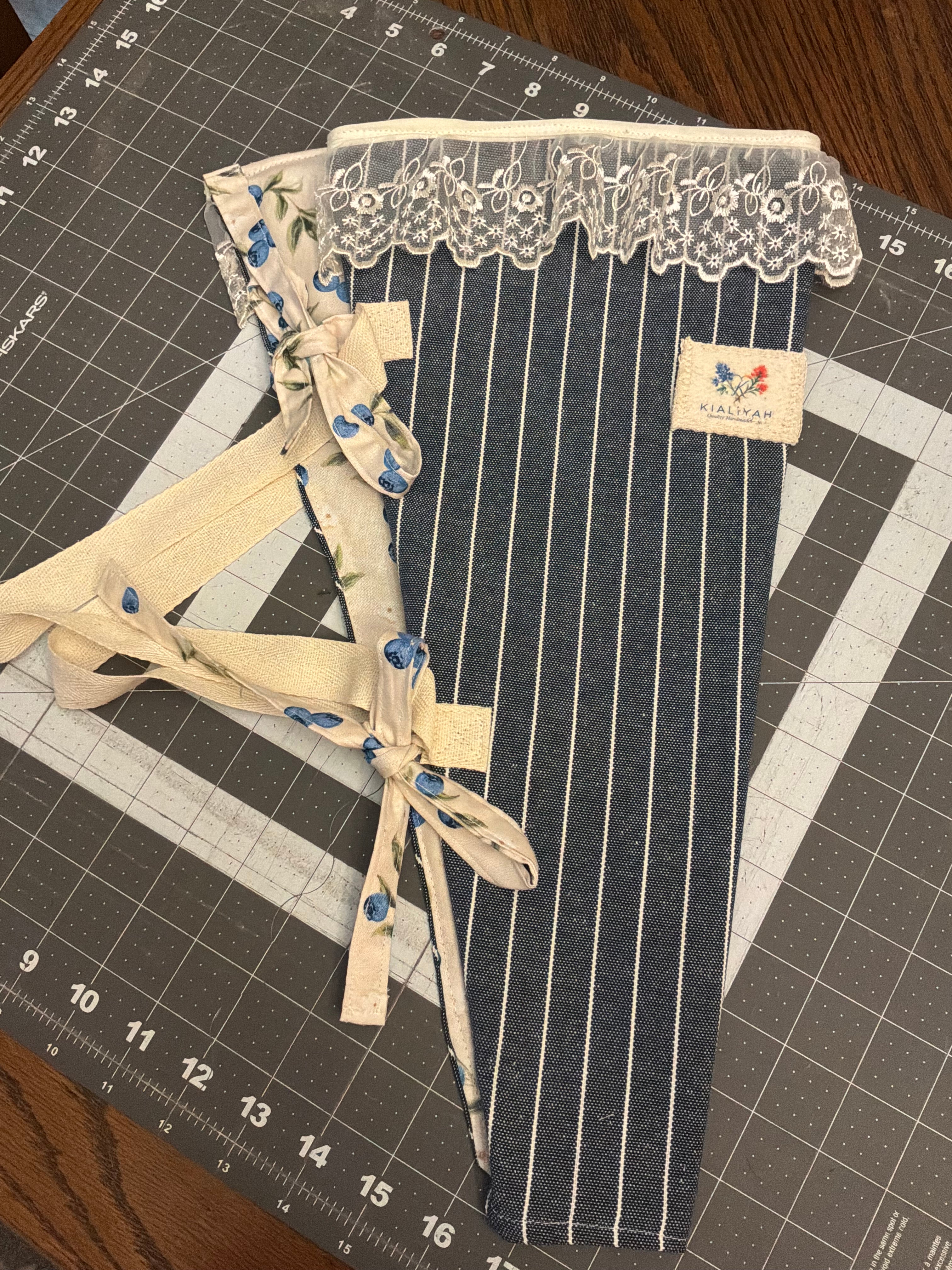 Indigo Pinstripe and Berry Bouquet Wrap canvas flower carrier featuring a deep blue and white pinstripe pattern with a white lace ruffle top and botanical berry patterned ties on a gray cutting mat.