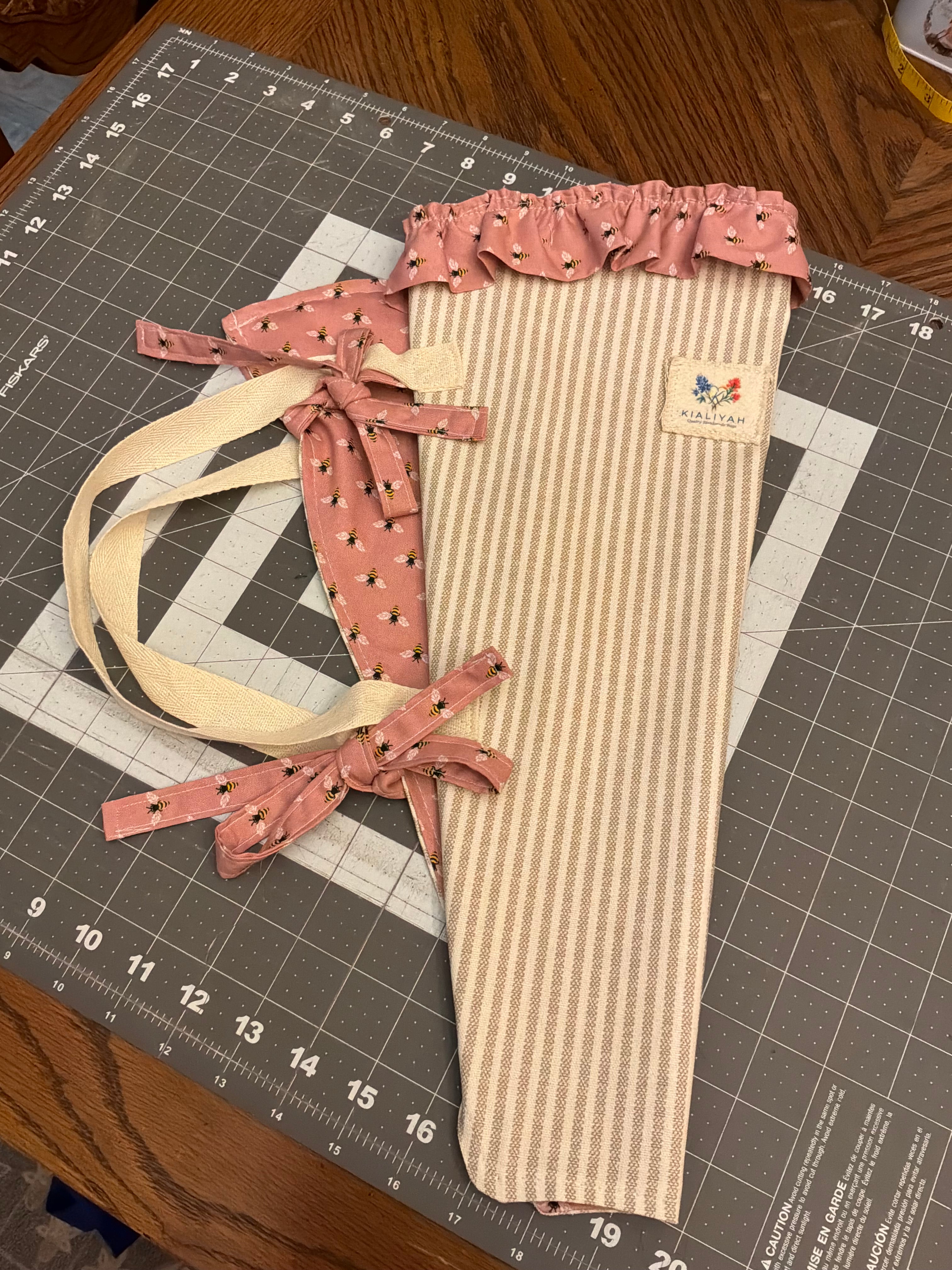 Prairie Stripe and Honeybee Bouquet Wrap canvas flower carrier featuring a warm neutral and cream ticking stripe pattern with a dusty rose honeybee ruffle top and matching bee-print side ties on a gray cutting mat.