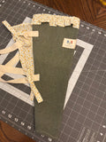 Texas Juniper and Blossom Bouquet Wrap canvas flower carrier featuring a solid dark juniper green canvas with yellow floral ruffles and cream shoulder straps on a gray cutting mat.