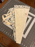 Wimberley Mist and Blossom Bouquet Wrap canvas flower carrier featuring a textured cream canvas with light blue floral ruffles and matching fabric side ties on a gray cutting mat.