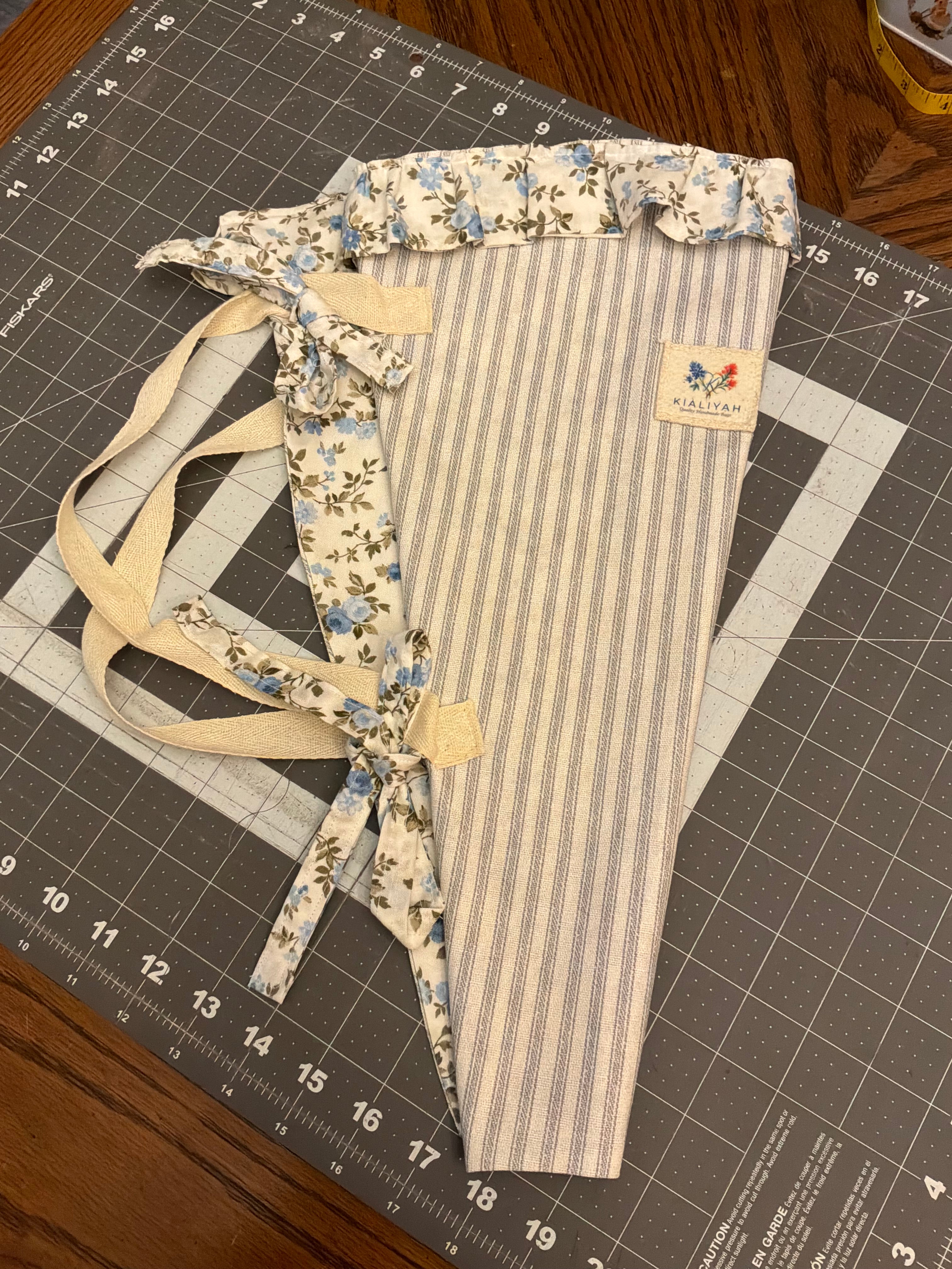 Coastal Bend Stripe and Blossom Bouquet Wrap canvas flower carrier featuring a slate-blue and cream ticking stripe canvas with light blue floral ruffles and matching fabric side ties on a gray cutting mat.