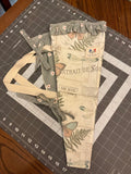 Post Oak Heritage Bouquet Wrap canvas flower carrier featuring a vintage cream botanical script fabric with butterflies and ferns, paired with a muted sage green daisy ruffle top and matching side ties on a gray cutting mat.