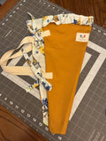 Guadalupe Sun and Monarch Bouquet Wrap canvas flower carrier featuring a vibrant marigold gold canvas with light blue butterfly and wildflower ruffles and matching fabric side ties on a gray cutting mat.