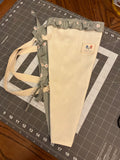 Sabinal Sage and Daisy Bouquet Wrap canvas flower carrier featuring a textured cream canvas with muted sage green daisy ruffles and matching fabric side ties on a gray cutting mat.