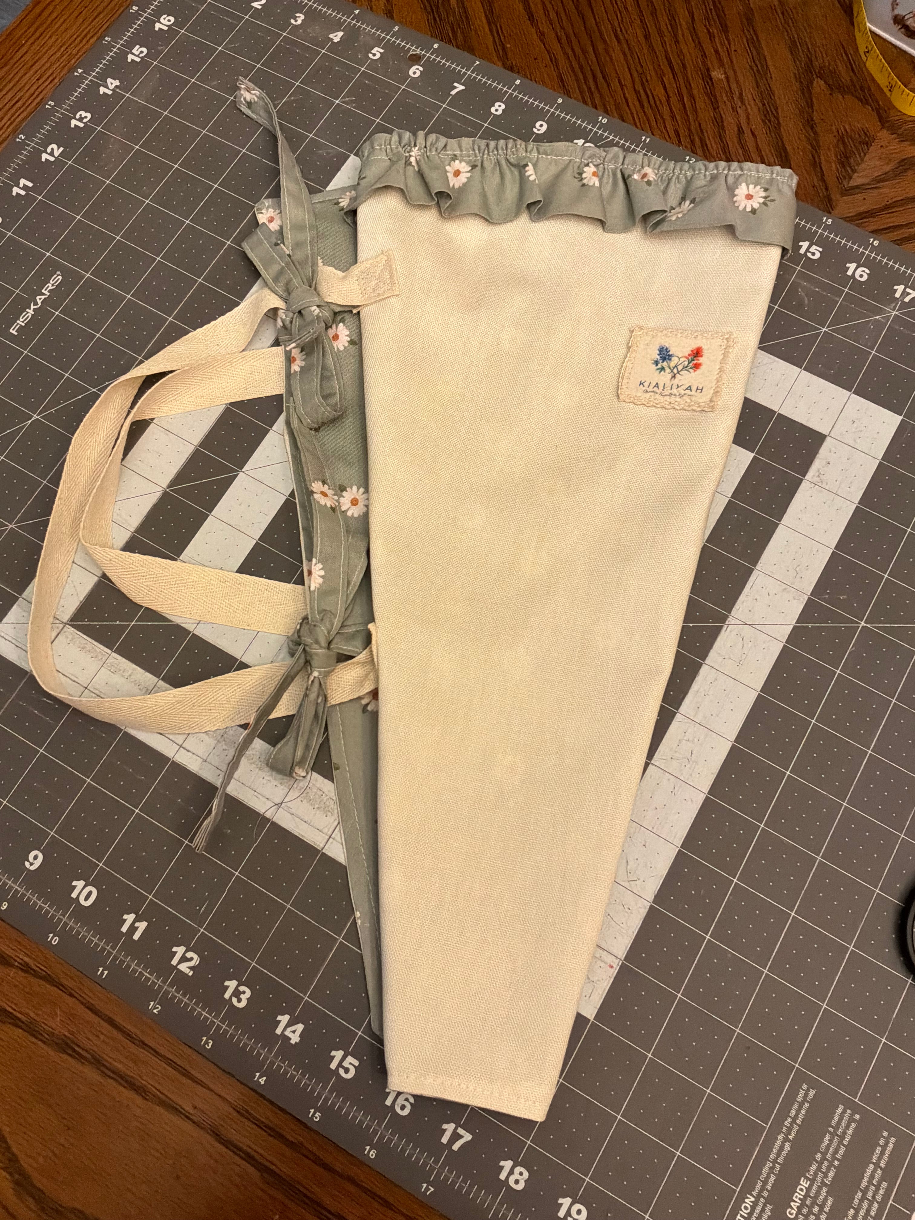 Sabinal Sage and Daisy Bouquet Wrap canvas flower carrier featuring a textured cream canvas with muted sage green daisy ruffles and matching fabric side ties on a gray cutting mat.