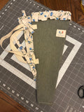 Medina River and Berry Bouquet Wrap canvas flower carrier featuring a solid dark juniper green canvas with cream blueberry ruffles and matching fabric side ties on a gray cutting mat.