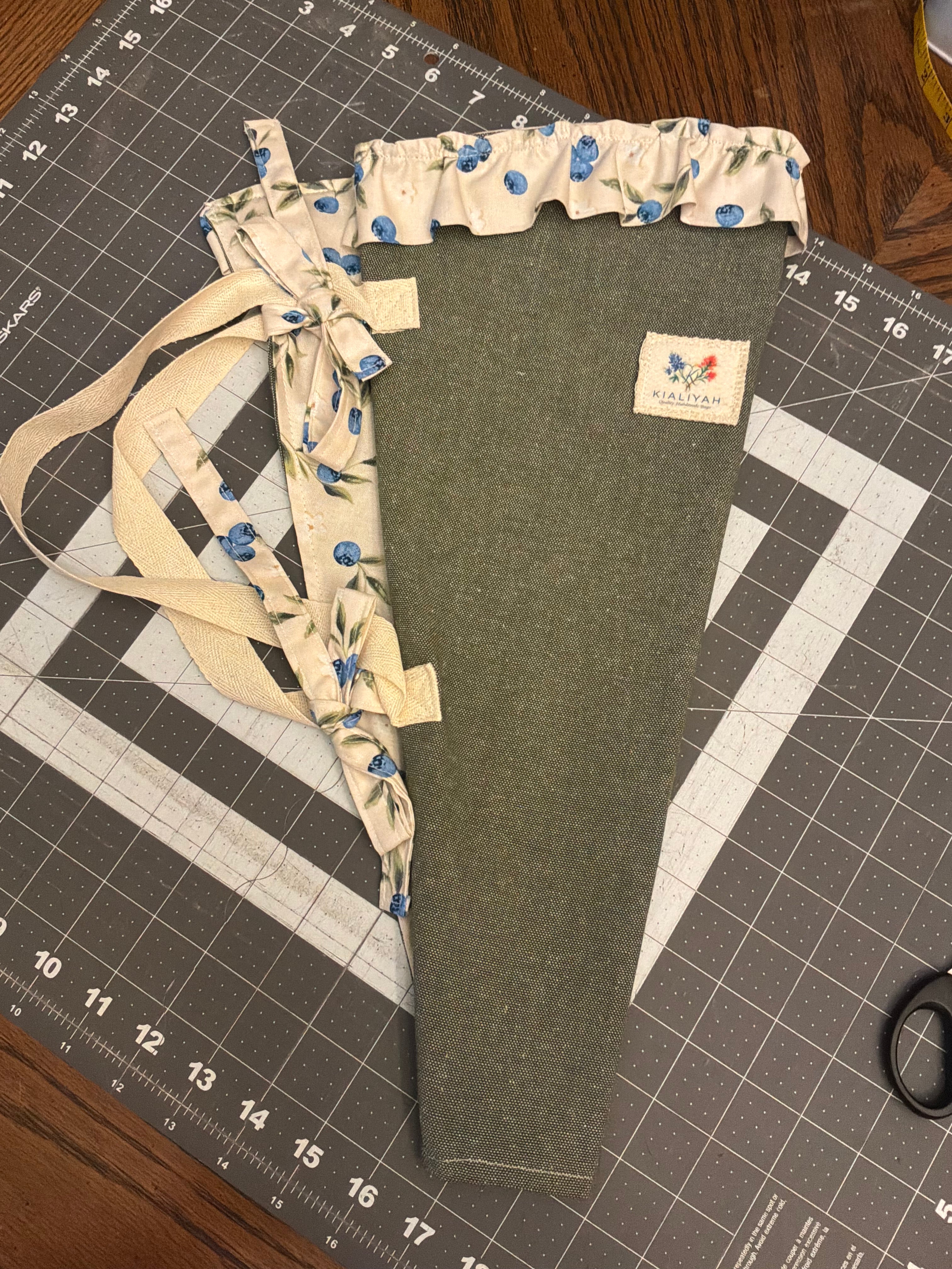 Medina River and Berry Bouquet Wrap canvas flower carrier featuring a solid dark juniper green canvas with cream blueberry ruffles and matching fabric side ties on a gray cutting mat.