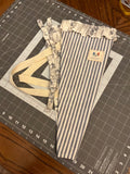 Bandera Toile and Indigo Stripe Bouquet Wrap canvas flower carrier featuring a deep navy and cream ticking stripe canvas with slate gray monochromatic floral toile ruffles and matching fabric side ties on a gray cutting mat.