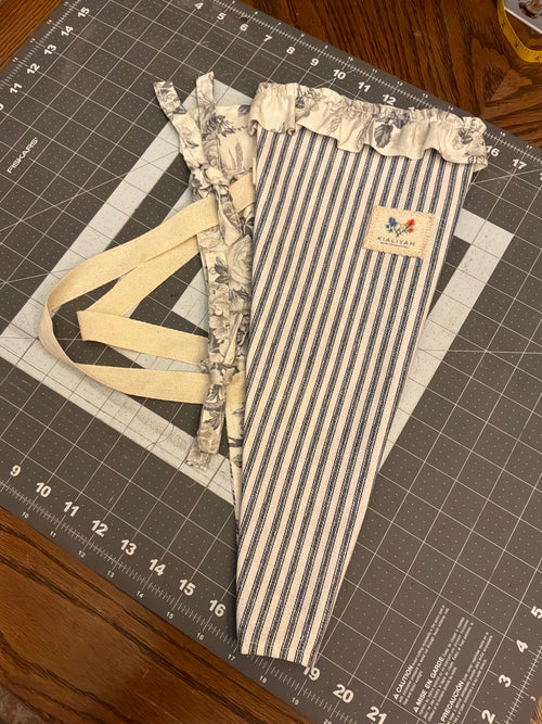 Bandera Toile and Indigo Stripe Bouquet Wrap canvas flower carrier featuring a deep navy and cream ticking stripe canvas with slate gray monochromatic floral toile ruffles and matching fabric side ties on a gray cutting mat.