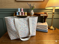 The Meadow Rose Quilted Market Tote featuring a dusty pink and cream floral print with sage green leaves, designed with plush diamond quilting, wide cream webbing straps, and matching fabric top ties, resting upright on a rustic wooden workshop table.