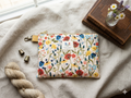 Handmade quilted wildflower print wristlet with gold hardware and yellow zipper pull on a linen background.