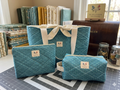 French Quarter Quilted Travel Bundle featuring a matching teal and cream geometric floral canvas tote bag with a cream bow, a boxy cosmetic case, and a flat zipper pouch on a gray cutting mat.