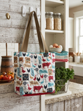 Country Pasture Quilted Carryall canvas grocery bag featuring a white chicken wire print with red cows, chickens, and windmills, wide olive green shoulder straps, and a central brand label hanging from a white hook.