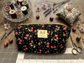 Black Cherry Jubilee Quilted Makeup Bag boxy cosmetic case featuring a black and white polka dot cherry print with vertical stitching and a gold zipper closure on a wooden workspace.