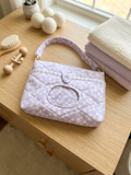 Purple Blossom Quilted Diaper Pouch showcasing a pastel lavender ditsy floral print with diamond quilting, an integrated wipe window, a purple heart snap closure, and a gingham wristlet strap resting on a wooden tabletop next to baby blankets.