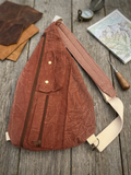 Rust Teardrop Sling Bag showcasing a terracotta canvas crossbody bag with multiple zippered pockets, a snap flap compartment, and a cream and burgundy gingham checkered patterned strap resting on a grey Fiskars cutting mat.