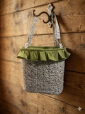 Sage and Violet Quilted Stroller Bag showcasing a cream and violet calico floral print fabric with a sage green polka-dot gathered ruffle top collar, hanging from an antique brass hook against a rustic wood plank wall.