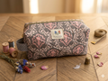 Vintage Damask quilted canvas makeup bag with a charcoal grey and blush pink damask pattern, a gold zipper, a grey polka dot side loop handle, and a central fabric brand label on a wooden table.