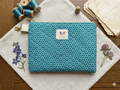 French Quarter Quilted Wallet canvas zipper pouch featuring a charcoal gray and blush pink damask print, a gray polka dot loop, and gold hardware on a wooden cutting board.