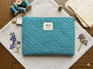 French Quarter Quilted Wallet canvas zipper pouch featuring a charcoal gray and blush pink damask print, a gray polka dot loop, and gold hardware on a wooden cutting board.