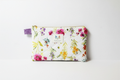 The Wildflower Garden Quilted Pouch & Small Wallet featuring a pink, purple, and amber floral print on white cotton fabric, designed with vertical channel quilting, a gold-tone top zipper with a matching fabric pull-tab, and a centered white KIALIYAH label.