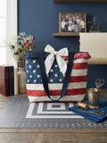 Old Glory Ruffle Market Tote showcasing an oversized diamond-quilted American flag handbag with wide navy straps, a split red and navy polka dot ruffle collar, and a white statement bow resting on a grey self-healing cutting mat.