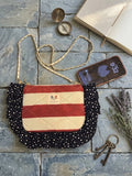 Patriot Stars Ruffle Cross Body Bag featured in IMG_20260701_055104.jpg showcasing a diamond-quilted red and white striped purse bordered by a navy star fabric ruffle, detailed with a gold chain strap on a slate stone background next to an open book and brass compass.