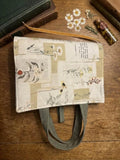 Pressed Floral Parchment Quilted Premium Bookcover showcasing a padded Bible sleeve with pressed daisy and vintage book page print, sage green handles, and a gold ribbon bookmark on a wood table.