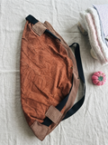 Rust Pull-Handle Market Tote featured in Pull Handle Tote Bag.png showcasing a terracotta canvas slouchy crescent shoulder bag with a main handle threaded through gathered cream and burgundy gingham fabric loops resting flat on a grey grid background.
