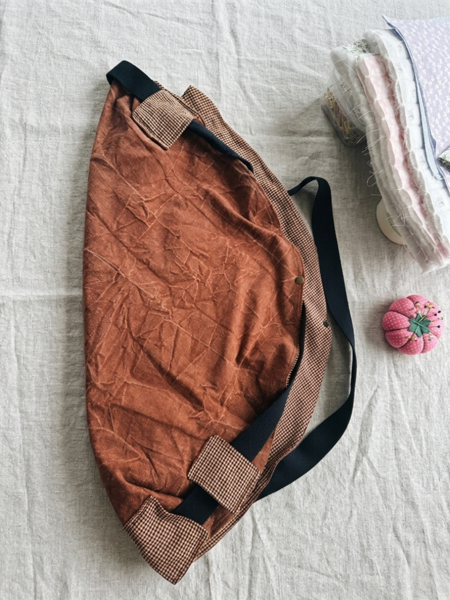 Rust Pull-Handle Market Tote featured in Pull Handle Tote Bag.png showcasing a terracotta canvas slouchy crescent shoulder bag with a main handle threaded through gathered cream and burgundy gingham fabric loops resting flat on a grey grid background.
