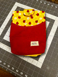 Handcrafted tablet sleeve featuring a solid red canvas front pocket, a sunny yellow upper panel printed with ladybugs and daisies, a matching snap closure tab, and an Elam & Co. fabric label resting on a cutting mat.