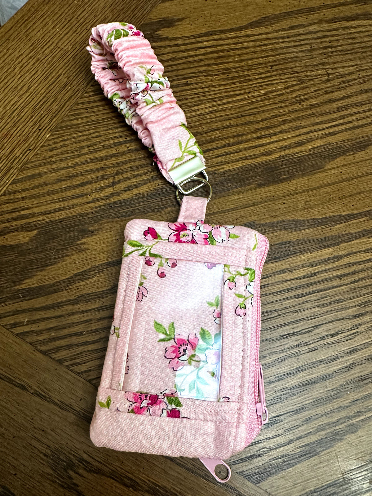 Back view of pink floral fabric wristlet ID wallet showcasing the clear front ID window slot and key ring wristlet attachment.