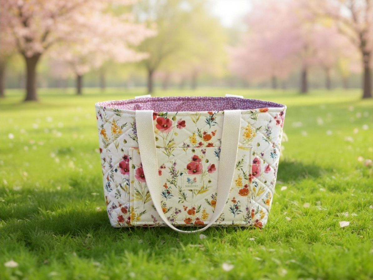 Floral-patterned tote bag on grass with cherry blossom trees in the background